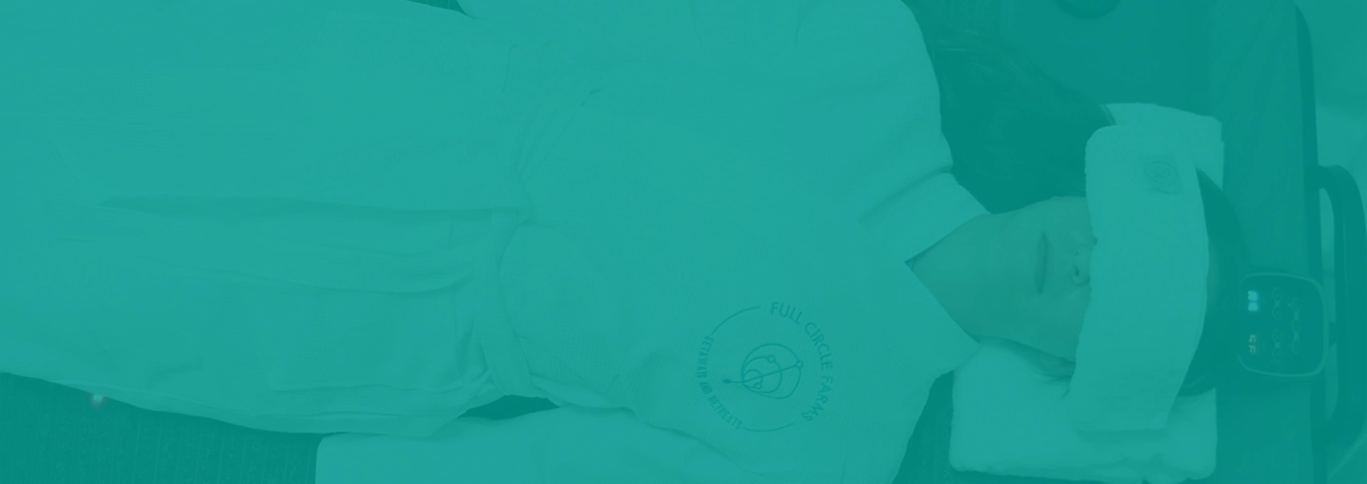 Person in a white spa robe with "Full Circle Farms" logo, a towel on their forehead, relaxing in a wellness setting.