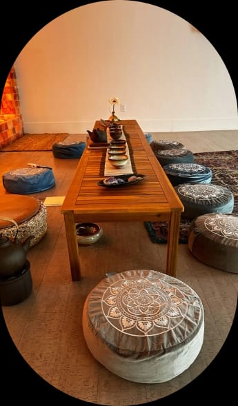 A meditative space with a long wooden table set for a tea ceremony, surrounded by floor cushions and illuminated by a warm salt lamp wall.